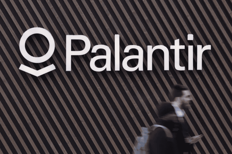 Palantir logo on a diagonal wood-panel wall with blurred people walking in front